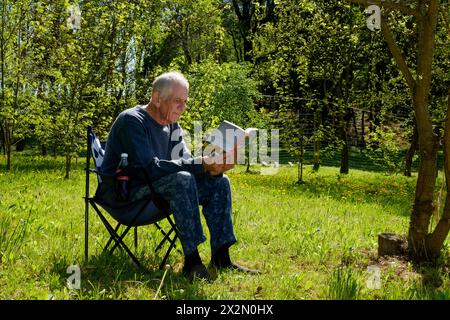 homme plus âgé se relaxant dans la chaise de jardin livre de lecture chaud printemps ensoleillé matin zala comté hongrie Banque D'Images