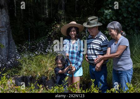 Jardinage avec des enfants. Les grands-parents avec leur fille et leur petit-fils latino-américain arrosent leur jardin. Hobbies et loisirs, style de vie, famille Banque D'Images