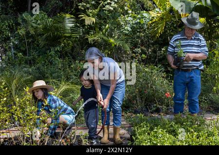 Jardinage avec des enfants. Les grands-parents avec leur fille et leur petit-fils latino-américain travaillent dans leur jardin. Hobbies et loisirs, style de vie, famil Banque D'Images