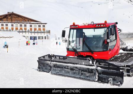 Machine rouge pour la préparation des pistes de ski dans les Alpes autrichiennes, le bâtiment et les touristes. Banque D'Images