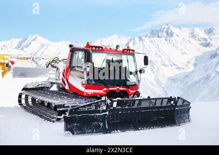 Machine rouge pour les préparations de pistes de ski dans les Alpes autrichiennes à l'arrière-plan des montagnes. Banque D'Images