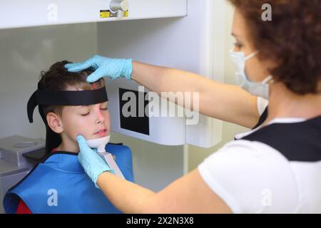 Dentiste en masque et gants prépare garçon à l'image de radiographie de mâchoire dans la clinique dentaire. Marquage laser sur le visage. Concentrez-vous sur le patient. Banque D'Images