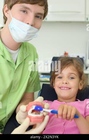 Dentiste montre à la patiente fille comment brosser correctement les dents. Pour plus de clarté, Docteur utilise une mâchoire artificielle. Concentrez-vous sur Docteur. Banque D'Images