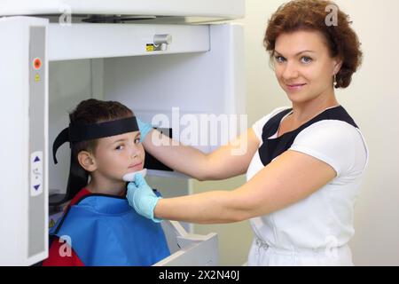 Dentiste prépare le garçon portant dans le tablier de plomb protecteur à l'image de radiographie de mâchoire dans la clinique dentaire et regarde la caméra. Concentrez-vous sur Docteur. Banque D'Images