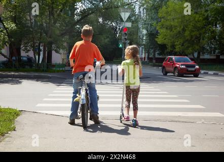 Garçon avec vélo et sa jeune sœur avec scooter stand avant de traverser au feu rouge Banque D'Images