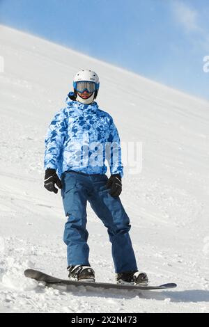 Snowboarder en costume de ski et casque se tient sur snowboard sur une colline enneigée Banque D'Images