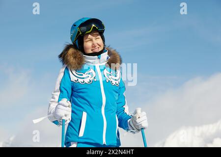 Jeune femme souriante en costume de ski bleu se tient debout et regarde, plissant au soleil Banque D'Images