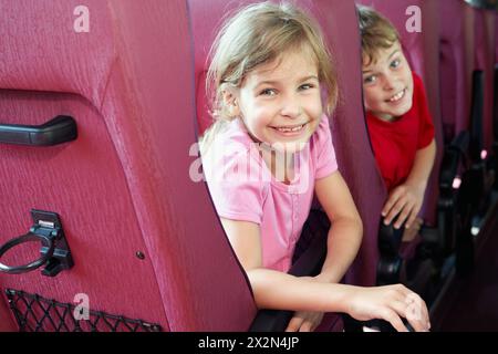 Garçon et fille souriants regardent depuis l'arrière des sièges dans le bus Banque D'Images