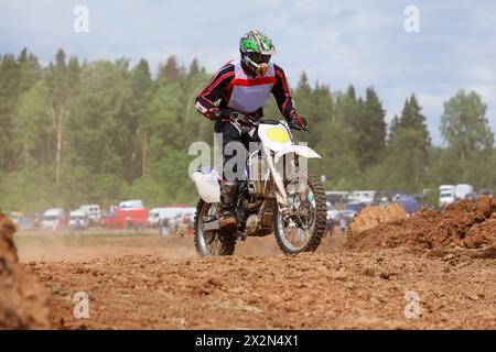 Jeune homme portant dans le casque sur la moto de terre saute sur les nids de poule boueux. Banque D'Images