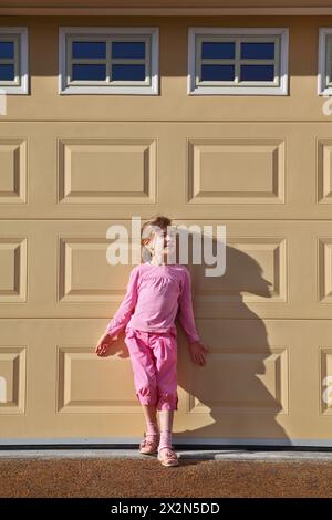 Petite fille portant en costume rose se tient près du mur jaune au jour ensoleillé. Banque D'Images