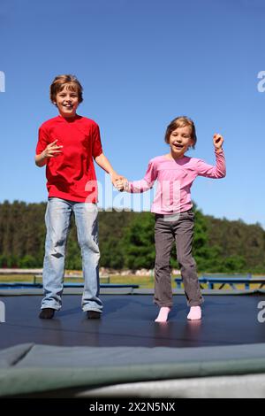 Frère et sœur souriants sautent sur le trampoline le jour ensoleillé d'été Banque D'Images