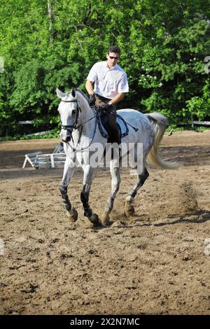 Jockey dans des lunettes chevauchant le cheval blanc sur l'hippodrome Banque D'Images