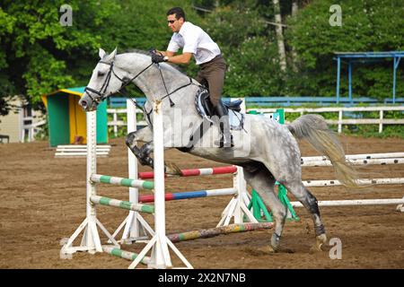 Jockey dans les lunettes sauter sur le cheval par-dessus la barrière sur l'hippodrome Banque D'Images