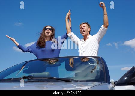 Jeune couple se tient debout, levant les mains en cabriolet et crie sur fond de ciel bleu Banque D'Images