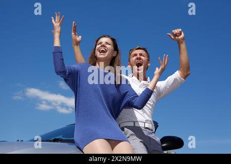 Jeune couple se tient debout, levant les mains en cabriolet et crie sur fond de ciel bleu vif Banque D'Images