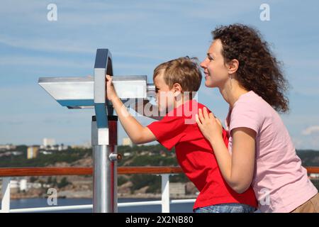La mère et le fils se tiennent sur le pont du navire ; le garçon regarde à travers des jumelles le paysage ; se concentrer sur la femme Banque D'Images