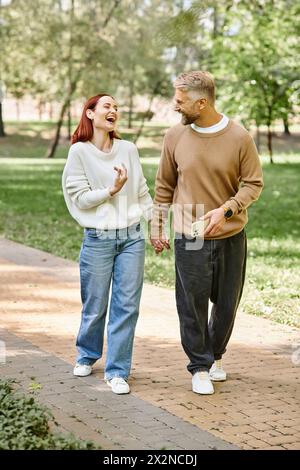 Un homme et une femme en tenue décontractée marchent ensemble sur un trottoir dans un parc. Banque D'Images