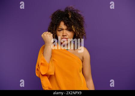 Femme afro-américaine élégante frappe une pose dans une robe orange sur un fond vibrant. Banque D'Images