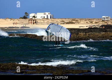 Homme plus âgé avec planche de feuille et voile à une plage rocheuse, El Cotillo, Fuerteventura, Îles Canaries, Espagne, Europe. Prise en février 2024 Banque D'Images