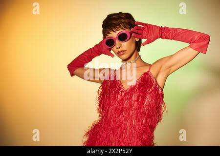 Une jeune femme à la mode dans une robe rouge et des gants rouges prend la pose sur un fond vibrant. Banque D'Images