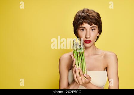 Une femme cache ludique son visage derrière un paquet d'asperges fraîches. Banque D'Images