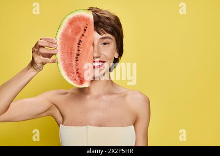 La jeune femme tient joyeusement la tranche de pastèque sur son visage. Banque D'Images