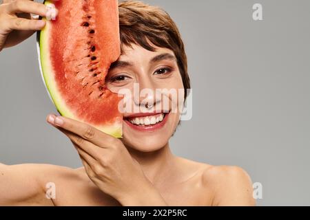 La jeune femme tient joyeusement la tranche de pastèque sur son visage. Banque D'Images