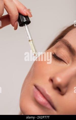 Belle jeune fille fraîche goutte à goutte huile cosmétique d'une pipette sur sa peau du visage, en gros plan. Beauté et soins de la peau Banque D'Images