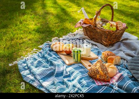 Couette de pique-nique et panier avec différents aliments, fruits, jus d'orange., yaourt et pain sur l'herbe verte Banque D'Images