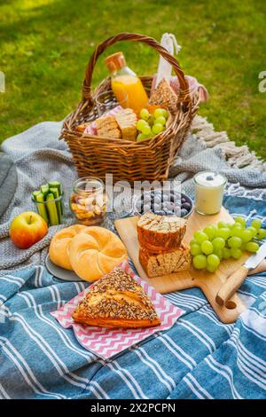 Couette de pique-nique et panier avec différents aliments, fruits, jus d'orange., yaourt et pain sur l'herbe verte Banque D'Images