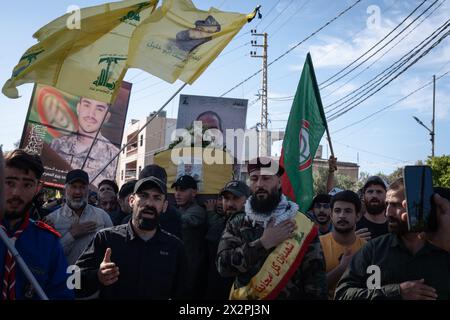 Une foule de personnes, y compris des combattants du Hezbollah chantent des slogans pendant les funérailles d'un autre combattant du Hezbollah, une foule en arrière-plan porte le cercueil à Mansouri. Le Hezbollah a organisé des funérailles dans le sud du Liban pour ses combattants tués dans une frappe israélienne. Les forces israéliennes et le groupe libanais Hezbollah ont intensifié leurs combats transfrontaliers, faisant craindre une escalade alors qu’Israël poursuit sa guerre contre Gaza et après l’échange de tirs entre l’Iran et Israël. Banque D'Images