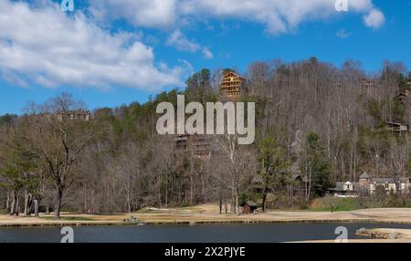 Plusieurs maisons sur le flanc d'une colline avec des arbres forestiers et un lac, sur une belle journée de printemps avec ciel bleu et des nuages blancs tortueux. Banque D'Images