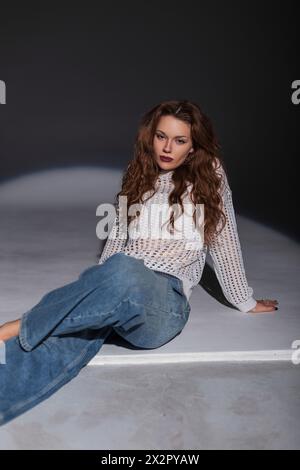 Élégant modèle de jeune fille dans Un pull blanc de mode avec Jean Vintage se trouve sur le sol dans le studio Banque D'Images