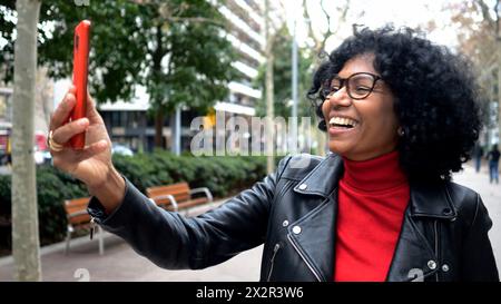 Femme afro-américaine d'âge moyen dans une ville faisant un appel vidéo dans une ville avec un téléphone portable Banque D'Images