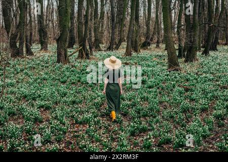 Femme portant un chapeau en osier et marchant au milieu des fleurs de Lily-of-the-Valley dans la forêt Banque D'Images