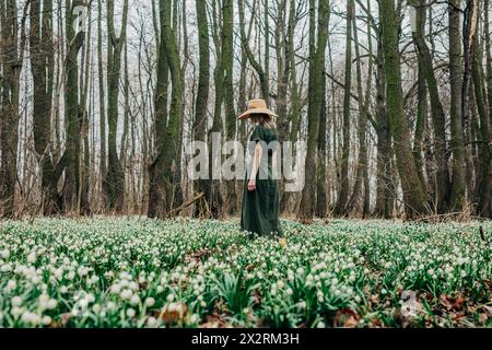 Femme marchant à travers les fleurs de Lily-of-the-Valley dans la forêt Banque D'Images