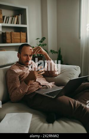 Indépendant inquiet utilisant un téléphone intelligent près de l'ordinateur portable au bureau à domicile Banque D'Images