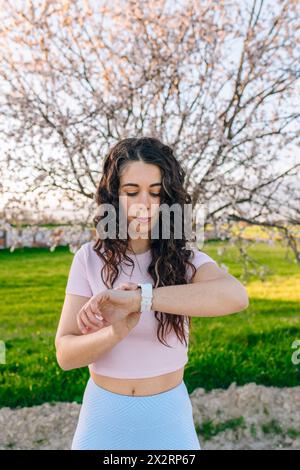 Femme vérifiant le téléphone intelligent debout devant l'arbre de fleur d'amande Banque D'Images