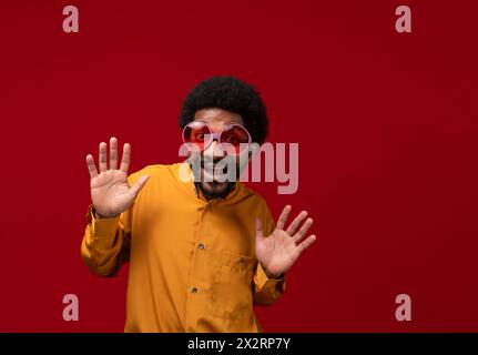 Homme heureux portant des lunettes de fête et faisant des gestes sur fond rouge Banque D'Images