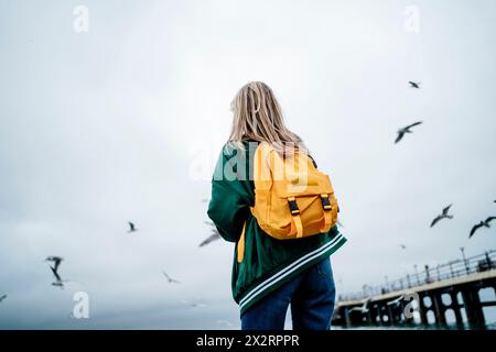 Femme nourrissant des mouettes volant dans le ciel par la mer Banque D'Images