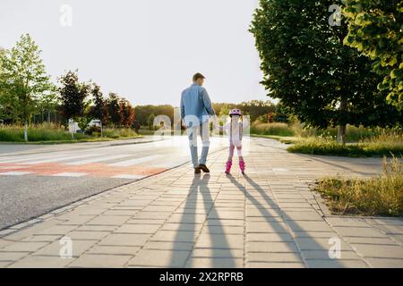 Homme tenant la main de sa fille faisant du patin à roulettes sur le trottoir Banque D'Images