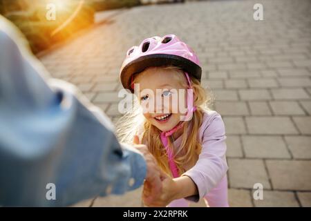 Fille souriante avec casque tenant la main du père sur le sentier Banque D'Images