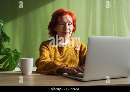 Femme d'affaires rousse senior utilisant un ordinateur portable travaillant à la maison Banque D'Images