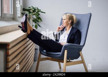 Femme d'affaires mûre réfléchie assise avec ordinateur portable sur fauteuil Banque D'Images
