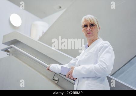 Médecin mature sérieux tenant le téléphone portable et debout sur l'escalier Banque D'Images