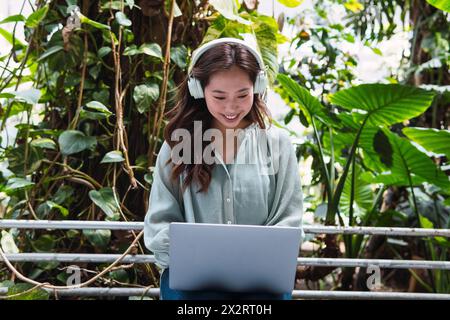 Femme souriante portant des écouteurs sans fil et utilisant un ordinateur portable Banque D'Images
