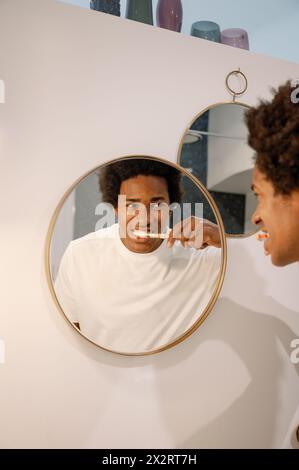 Homme se brossant les dents regardant le reflet sur le miroir dans la salle de bains Banque D'Images
