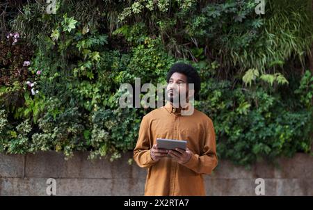 Homme debout avec tablette PC devant le mur végétal vert Banque D'Images