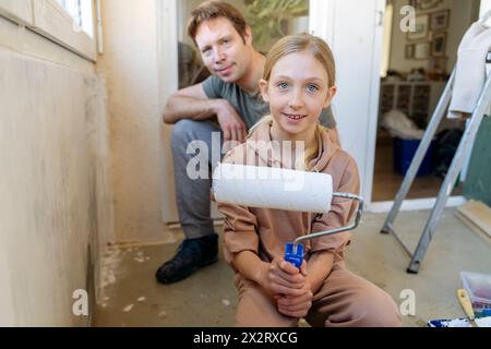 Fille tenant le rouleau de peinture avec le père en arrière-plan à la maison Banque D'Images