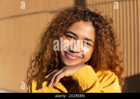 Heureuse belle jeune femme aux cheveux bouclés avec des autocollants jaunes en forme de coeur sur les joues Banque D'Images